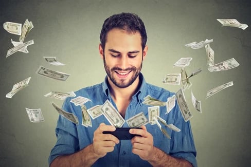 Technology online banking money transfer, e-commerce concept. Happy young man using smartphone with dollar bills flying away from screen isolated on gray wall office background- Flawless Inbound